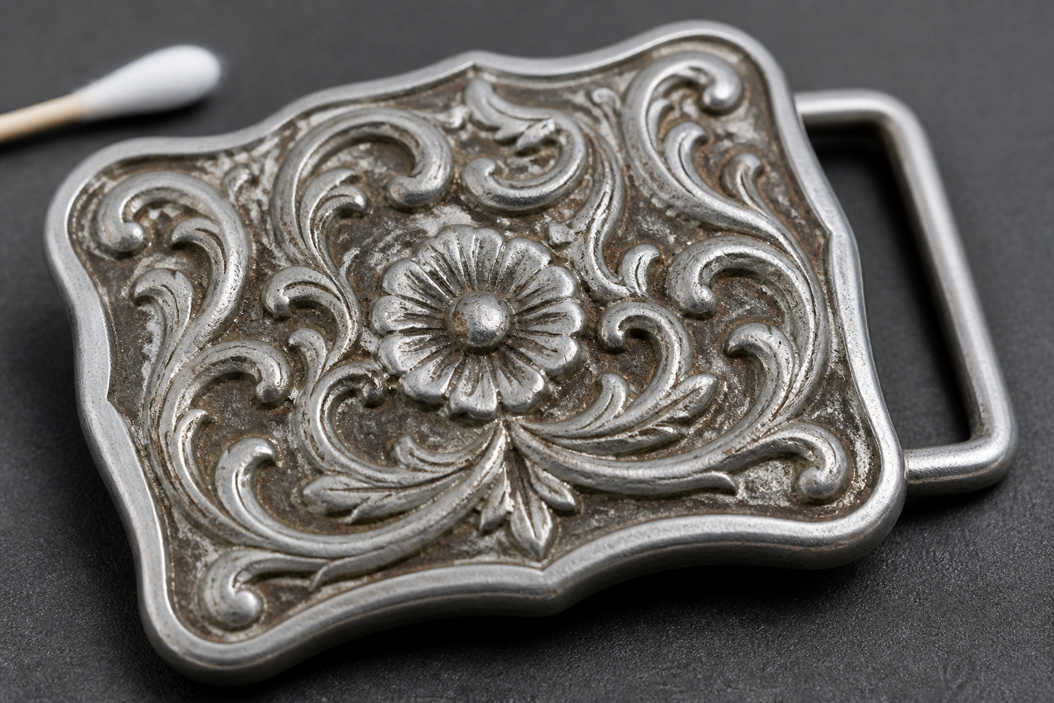Brown-gray Tripoli-type residue trapped in the relief of a silvery-gray pewter or zamak cast buckle.