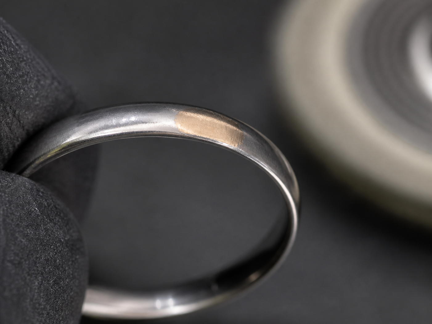 A bounded worn-through patch on a plated ring edge reveals warmer base metal beneath the intact surface layer.