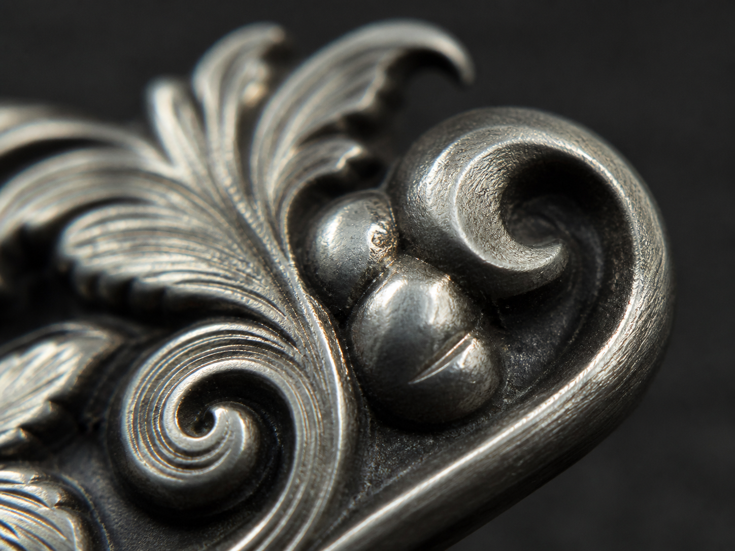 Ornate metal relief with one softened rounded detail beside sharper engraved ridges.