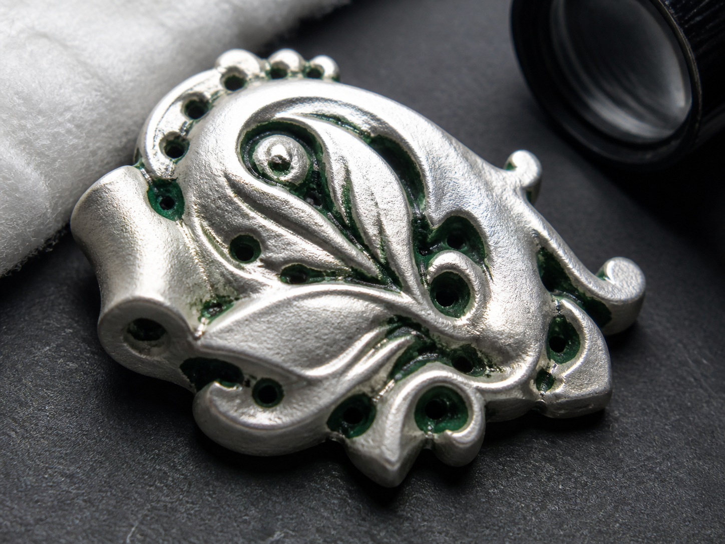 Dark green residue localized in multiple holes and recessed channels of a clean silvery fitting.