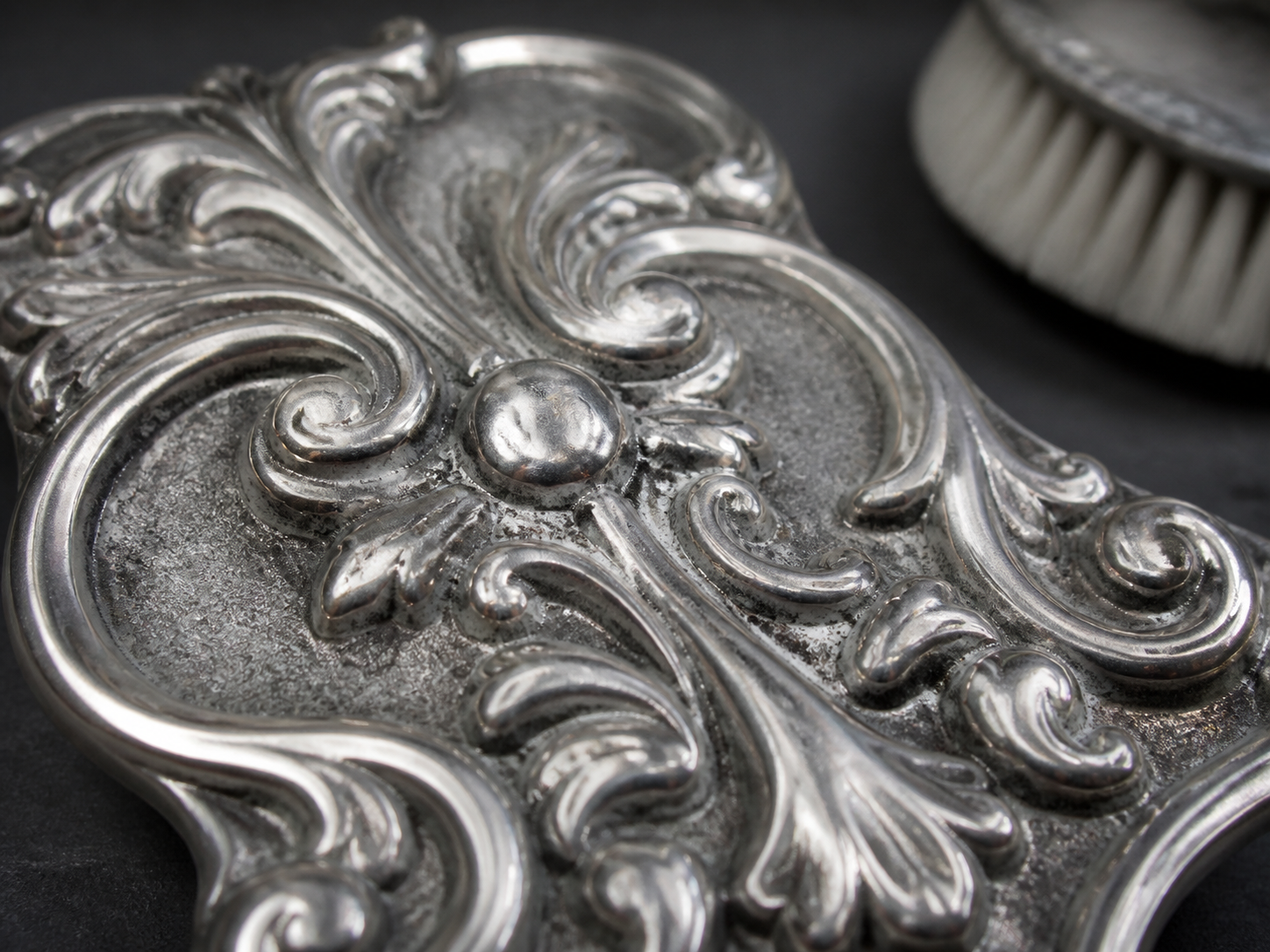 An ornate metal relief with bright raised edges and visibly dull recessed fields beside a small brush.