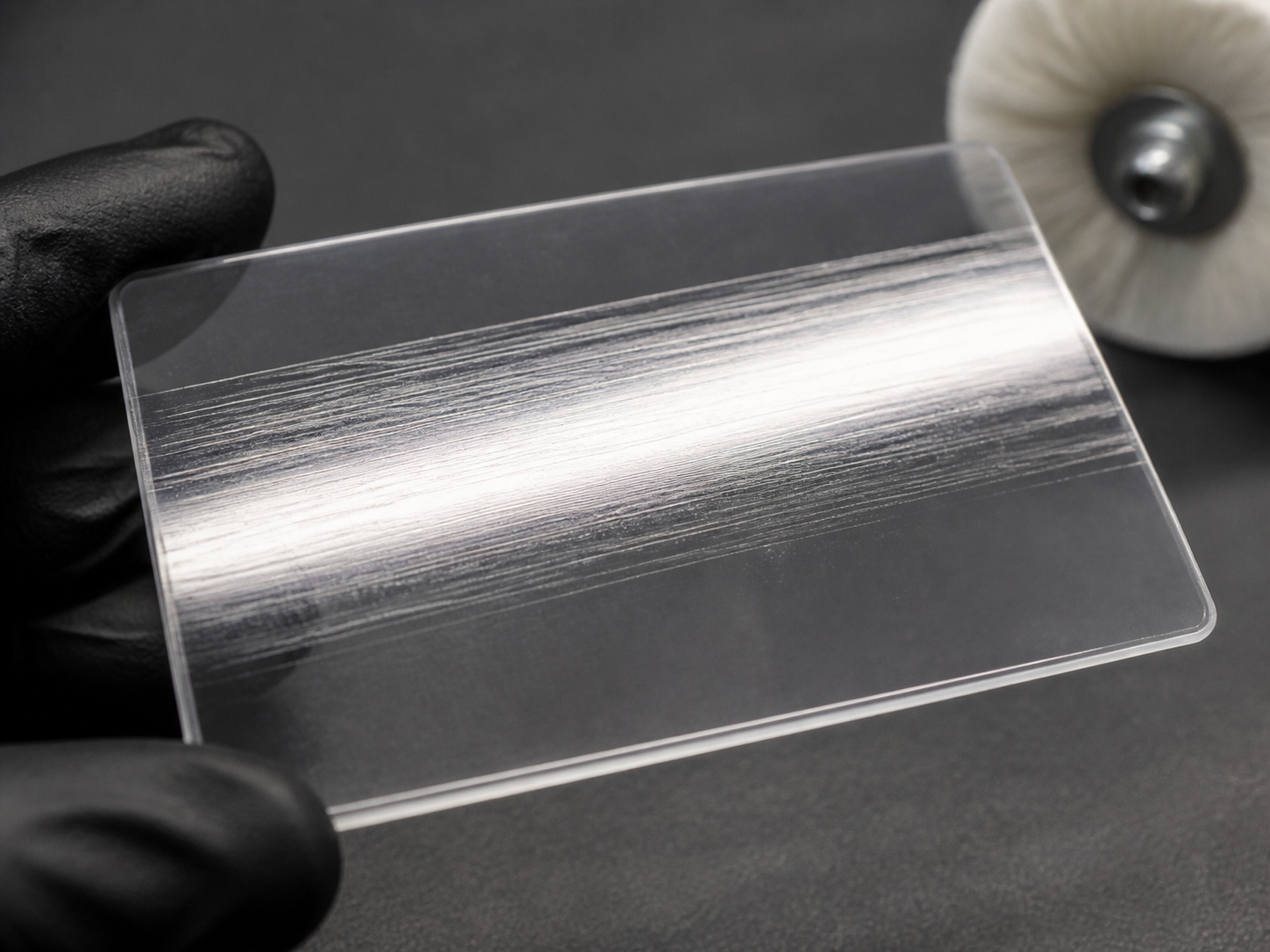 A clear polymer coupon with a glossy worked band where fine parallel scratches remain visible.
